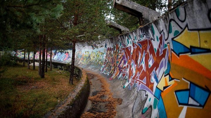 Znečištěný prostor s troskami, nečistotami a zdobený graffiti. V blízkosti olympijské vesnice se nachází oblast určená pro migranty.